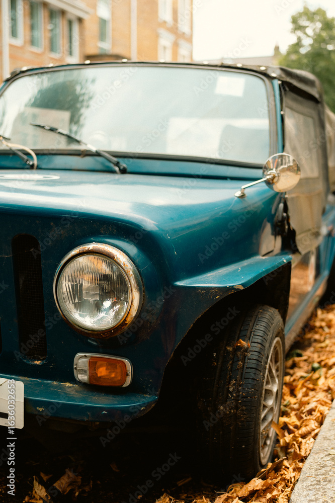 Fototapeta premium Front close-up of a vintage blue convertible parked on a leaf-covered street in Chiswick, West London