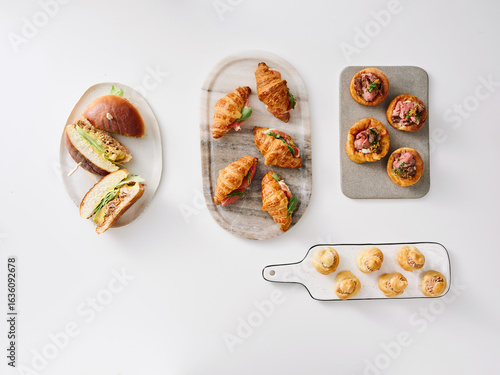 A variety of freshly baked pastries and sandwiches are beautifully arranged on platters. The scene captures an inviting brunch setting that highlights culinary artistry and presentation