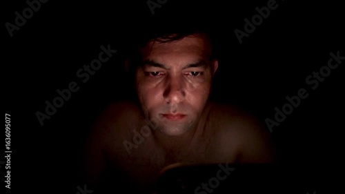 Close up, a tired man in bed scrolls endlessly on his mobile phone, struggling with insomnia, anxiety and overthinking as he watches social media late into the night