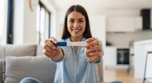 A woman holds a positive pregnancy test, celebrating her good news at home.