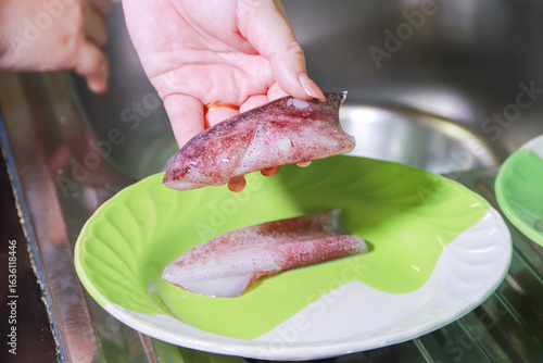 Hand Holding Cleaned Squid Body Above Green and White Plate