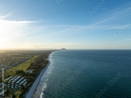 Wallpaper Mural Aerial view of the coastline where the serene turquoise sea meets the sandy shore, as the distant Mauao mountain stands guard, Papamoa, Bay of Plenty Region, New Zealand. Torontodigital.ca