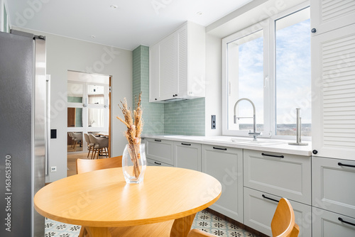 Modern kitchen with a round wooden table and stylish decor offers a serene cooking space with natural light in a contemporary apartment