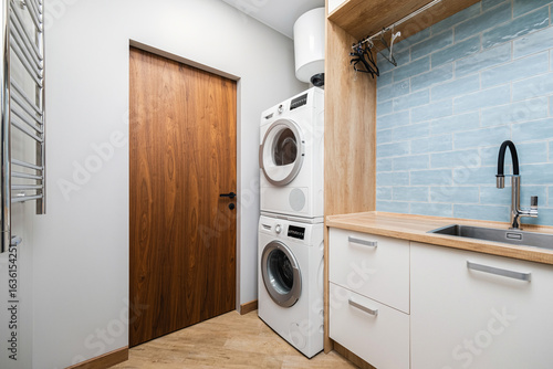 Modern laundry room featuring washer and dryer with wooden elements and blue tiled backsplash at home