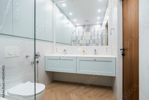 Modern bathroom interior featuring glass shower, wooden flooring, and stylish cabinetry in a contemporary design