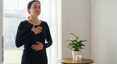 A calm woman with closed eyes practices a mindful breathing exercise with hands on her chest and belly.