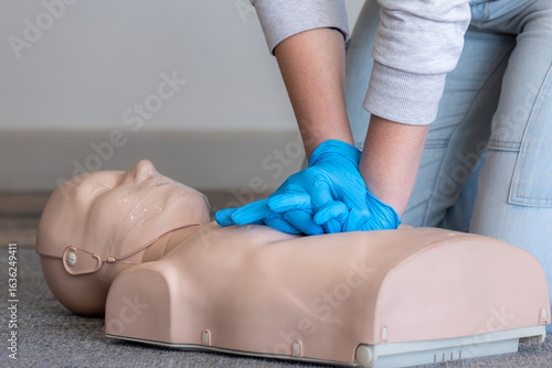 Closeup of the hands of a female first aid instructor demonstrating correct posture and hand position for administering chest compressions on a Basic Life Support (BLS) CPR manikin.