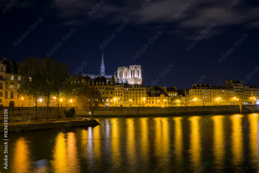 Fototapeta premium Illuminated Parisian Skyline with Notre-Dame Cathedral Reflected in the Seine River at Night