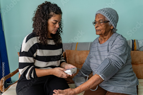 Foto Candid Moment of Latina Woman Checking Blood Pressure of Afro Grandmother at Hom