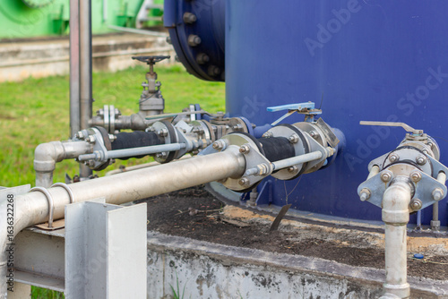 Industrial plumbing system featuring metal pipes valves and a large blue tank showcasing essential infrastructure components for water management or chemical processing at a plant or factory setting