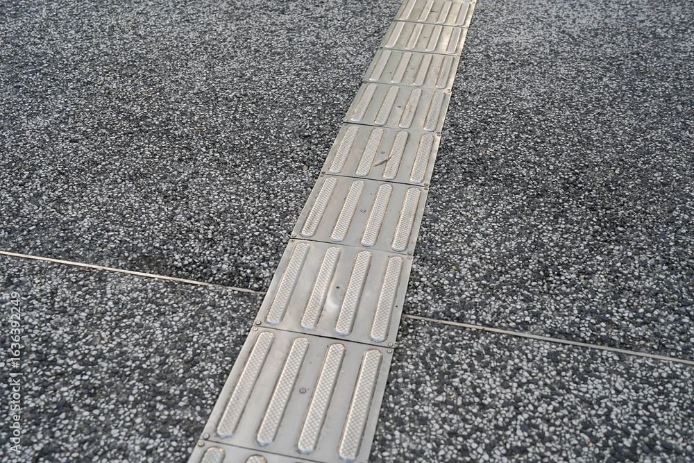 Fototapeta premium Tactile Paving Pathway on Cobblestone Road – Accessible Sidewalk for the Visually Impaired