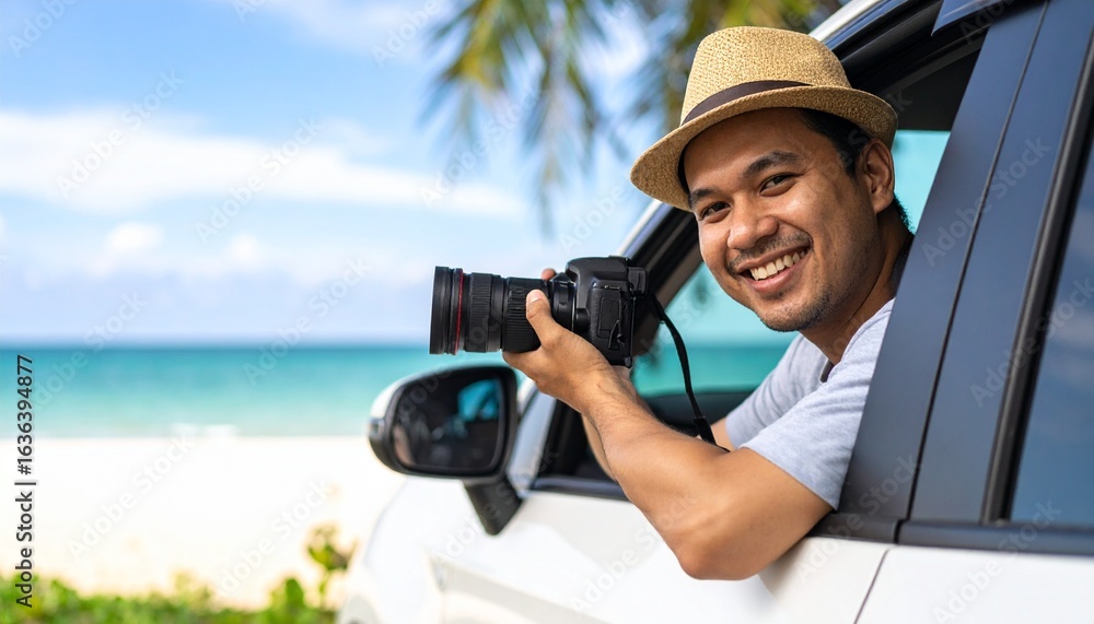 Obraz premium Happy young man smiling and holding a camera out of a car window, with a tropical beach view