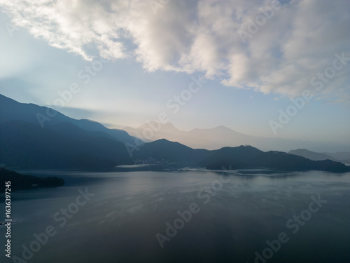 Aerial view of a serene lake reflecting mountains and clouds at sunrise. Misty atmosphere.