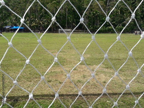 A close-up of a soccer goal on a grassy field. The background reflects the essence of local sports or a soccer field in a village.