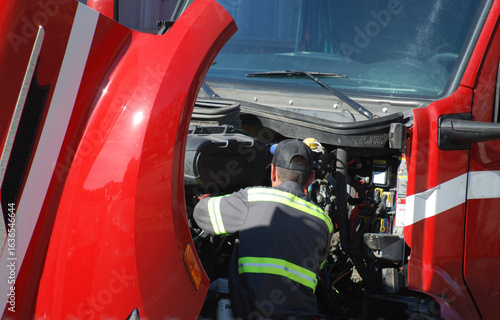 Diesel mechanic working on engine of red truck.