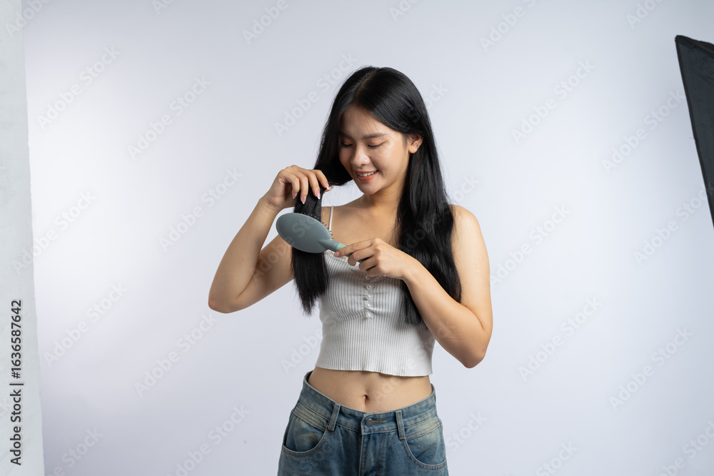 Smiling woman brushing her long dark hair with a blue hairbrush in a bright studio setting Smiling woman brushing her long dark hair with a blue hairbrush in a bright studio setting