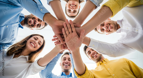 A low-angle view of a diverse team putting their hands together in a huddle, smiling. Perfect for symbolizing unity, teamwork, and shared success
