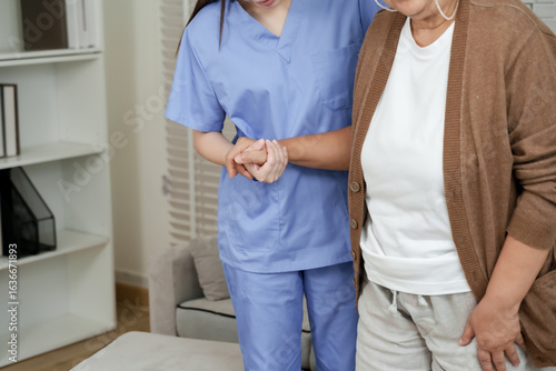 Close up of hand support from female asian physiotherapist during elderly walking practice with senior asian woman for strength recovery and movement improvement therapy