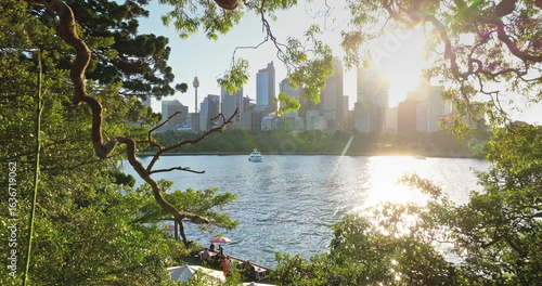 Australia, Sydney: Warm sunlight reflect on water, city skyline modern buildings in background, framed by green lush trees window, creating scenic urban nature view. Drone . Travel background