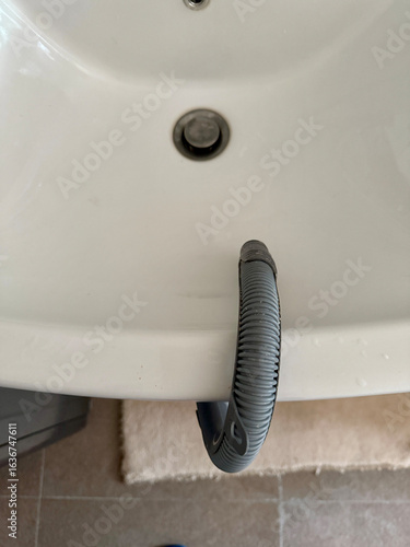 Macro view of a gray flexible drain tube leading to a white ceramic sink, a way of using washing machine without water drainage, straight view