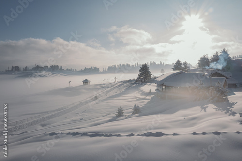 Wallpaper Mural Aerial view of snow-covered cabins nestled amidst the serene, white landscape, where the sun casts a warm glow over the frosty scenery, Gulmarg, Jammu and Kashmir, India. Torontodigital.ca