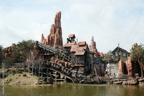 Rustic Western Theme Park Mountain with Wooden Roller Coaster and Scenic Lake View on a Bright Day