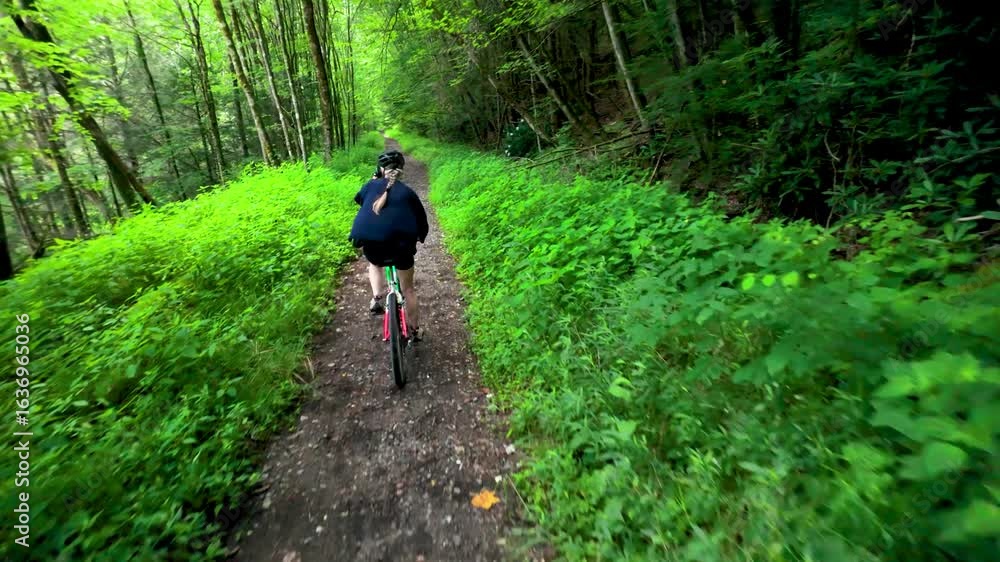 A mature woman enjoys biking along a rail trail path in a vibrant forest in Blackwater Canyon, Thomas, West Virginia, surrounded by lush greenery and natural beauty. A mature woman enjoys biking along a rail trail path in a vibrant forest in Blackwater Canyon, Thomas, West Virginia, surrounded by lush greenery and natural beauty.