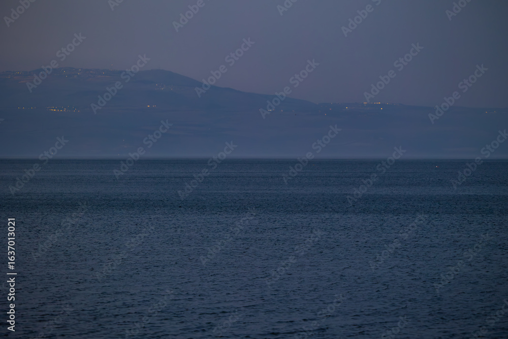 Obraz premium Evening twilight views of the Sea of Galilee in Israel with calm waters, distant mountains, boats, and serene blue tones creating a peaceful atmosphere