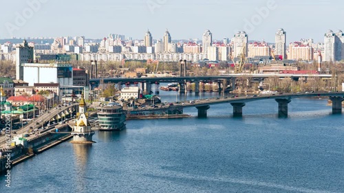 Timelapse. View of the panorama of Kyiv with traffic on the bridge over the Dnieper River, on the river bank, urban architecture and residential buildings under a clear sky
