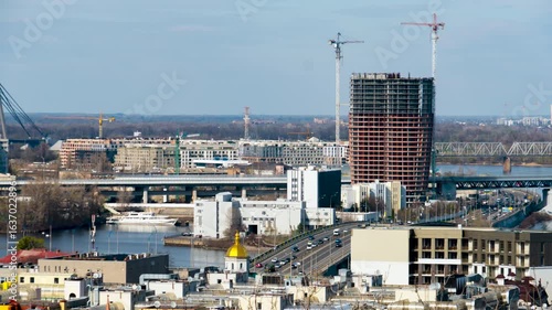 Kyiv, Ukraine - 04.13.2025:  Timelapse. Kyiv city panorama with traffic, modern high-rise building under construction, cranes, bridges and river view on a sunny day