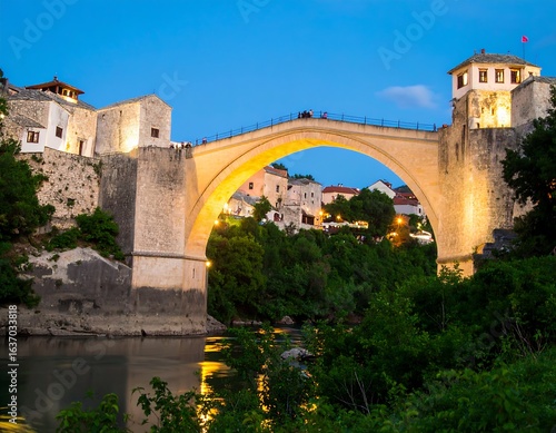 Stone arch bridge at dusk over river, town nestled in hills
