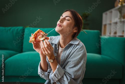 Fotografie Young woman enjoying pizza at home: licking finger with closed eyes