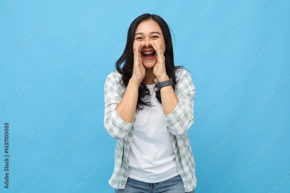 Young asian woman smiling, wearing casual clothes, shouting sharing hot news about sale discount with hand near mouth, isolated on blue background. Young asian woman smiling, wearing casual clothes, shouting sharing hot news about sale discount with hand near mouth, isolated on blue background.