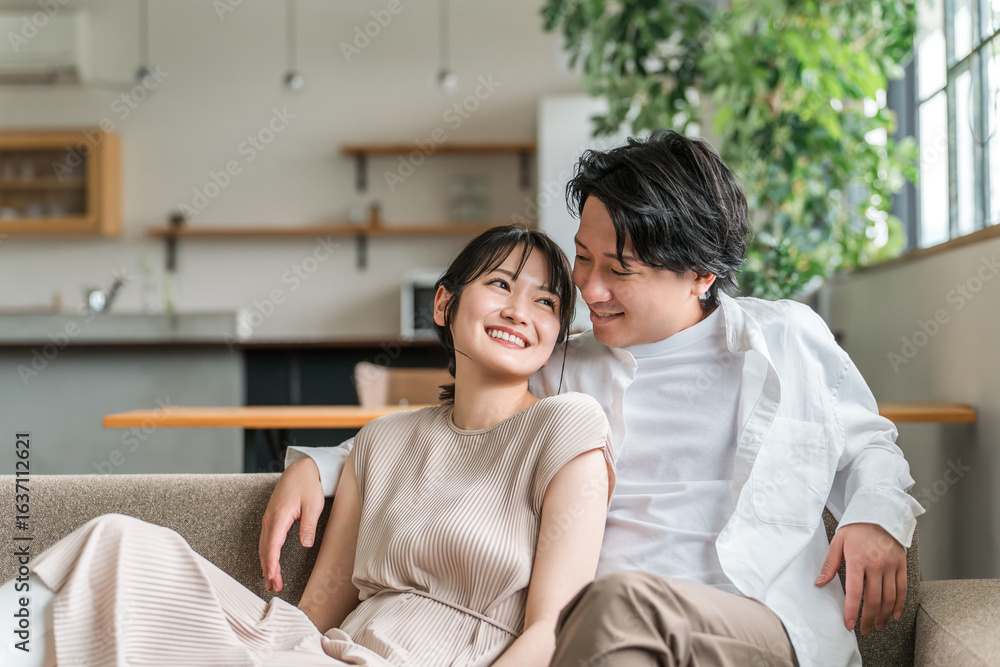 Fototapeta premium 家のリビングでソファーに座る仲良しな若いアジア人夫婦 