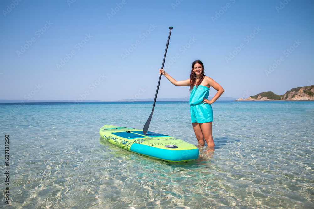 Fototapeta premium Sup boarding. An attractive young girl with sup board on the background of the sea. The concept of active lifestyle and surfing.
