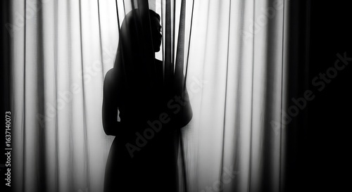 Silhouette of a woman standing behind curtains in a dark room expressing mystery and privacy and contemplating life in monochrome