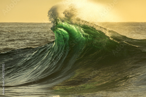 A powerful ocean wave breaks above a reef in the warm glow of sunrise on the South Coast of New South Wales, Australia.