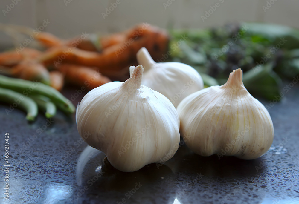 Obraz premium Three vibrant garlic bulbs on a dark surface, ready for healthy, organic, and real food recipes. Perfect for diet and clean eating visuals