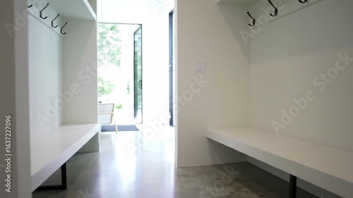 Interior view of a white wall with hooks and a bench in a modern house hallway design style