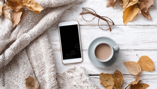 Cozy autumn scene with smartphone, coffee, and leaves on a white wooden table