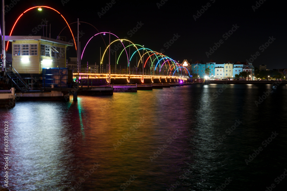 Fototapeta premium Vista noturna de Willemstad, Curaçao, com fachadas históricas iluminadas refletindo nas águas calmas, capturando o charme e a beleza da arquitetura caribenha.