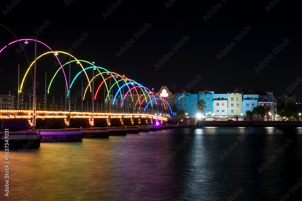 Obraz premium Vista noturna de Willemstad, Curaçao, com fachadas históricas iluminadas refletindo nas águas calmas, capturando o charme e a beleza da arquitetura caribenha.