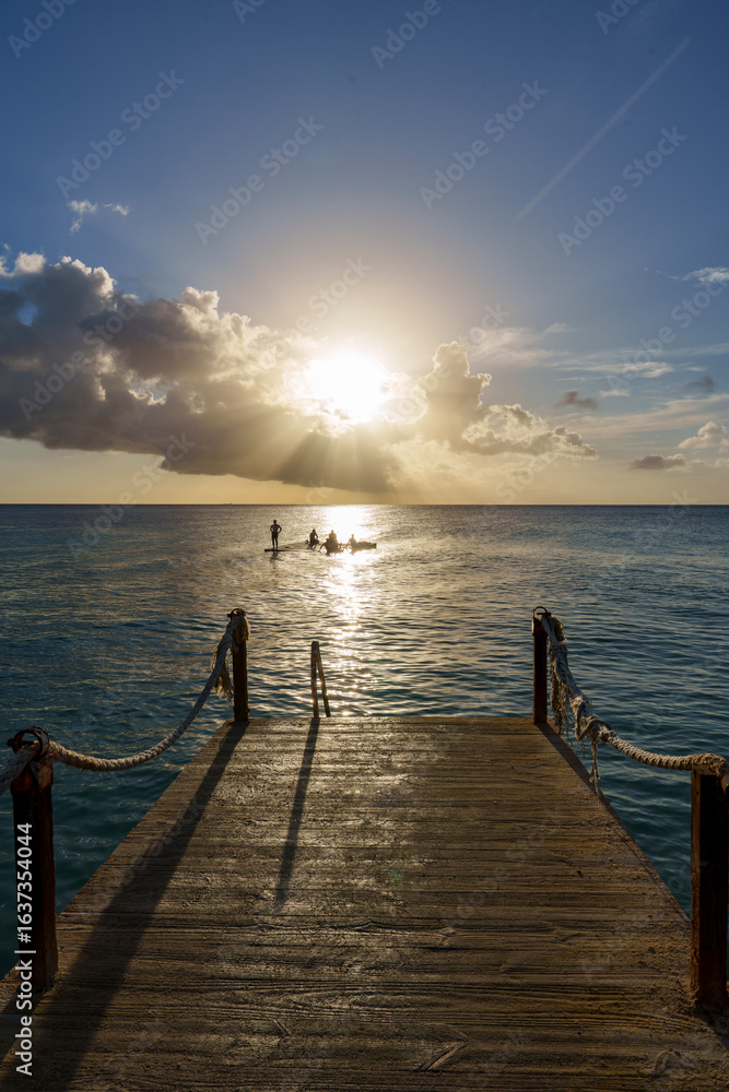 Fototapeta premium Pier de madeira no Caribe em Curaçao ao pôr do sol, com raios de luz refletindo no mar calmo e cenário tropical sereno, ideal para transmitir paz e beleza natural