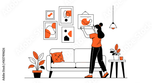 Woman hangs artwork on wall above sofa in living room with plants and light fixture