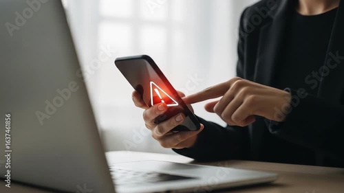 Woman taps a smartphone displaying a red exclamation point warning A nearby laptop suggests a technology issue is at hand possibly related to security