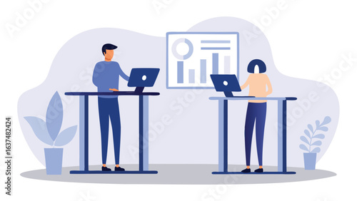 Two people working on laptops at standing desks in an office with a chart on the wall behind them