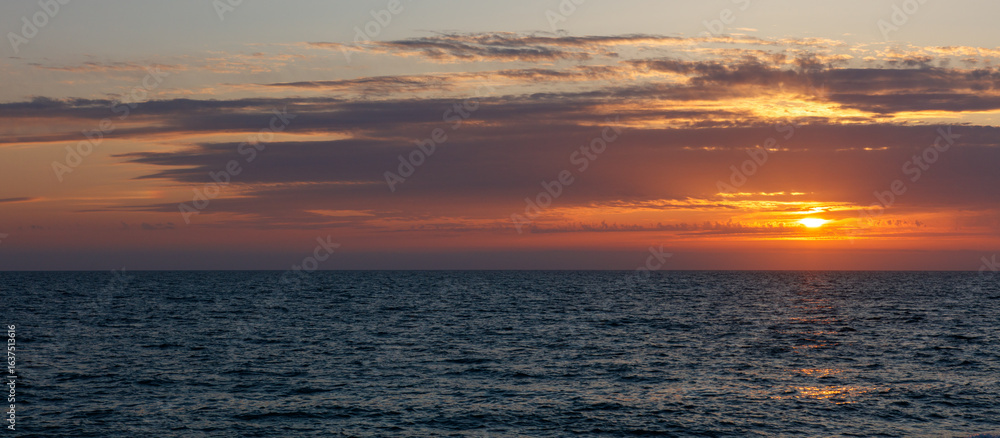 Obraz premium The sky is a beautiful orange color as the sun sets over the ocean