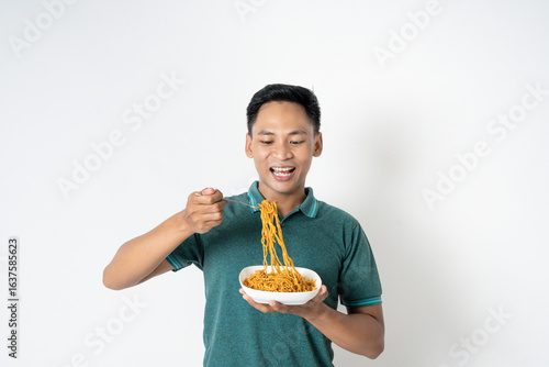 Bild auf Leinwand A man wearing a green shirt eagerly eats instant noodles from a bowl, clearly enjoying the meal