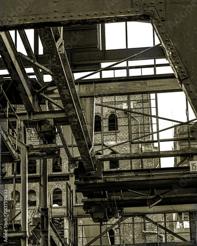 Wallpaper Mural Durch die verrosteten Stahlträger und Balken hindurch sieht man die Backsteinfassaden, die einst voller Leben waren. Die Perspektive betont die schiere Größe und Komplexität dieser verlassenen Orte. Torontodigital.ca