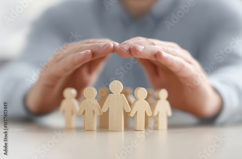 Businessman is protecting wooden figures of people with his hands, insurance and patronage concept